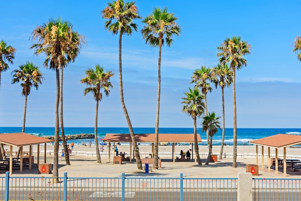 A beach with palm trees, beach huts, and a clear blue sky.