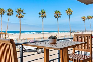 A wooden table with a potted plant, overlooking a beach with palm trees and a clear blue sky.