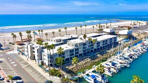 A coastal hotel with multiple floors, a marina with boats, and a beach in the background.