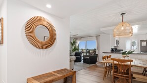 A modern living room with a wooden bench, a round mirror, and a dining area with wooden chairs and a table.