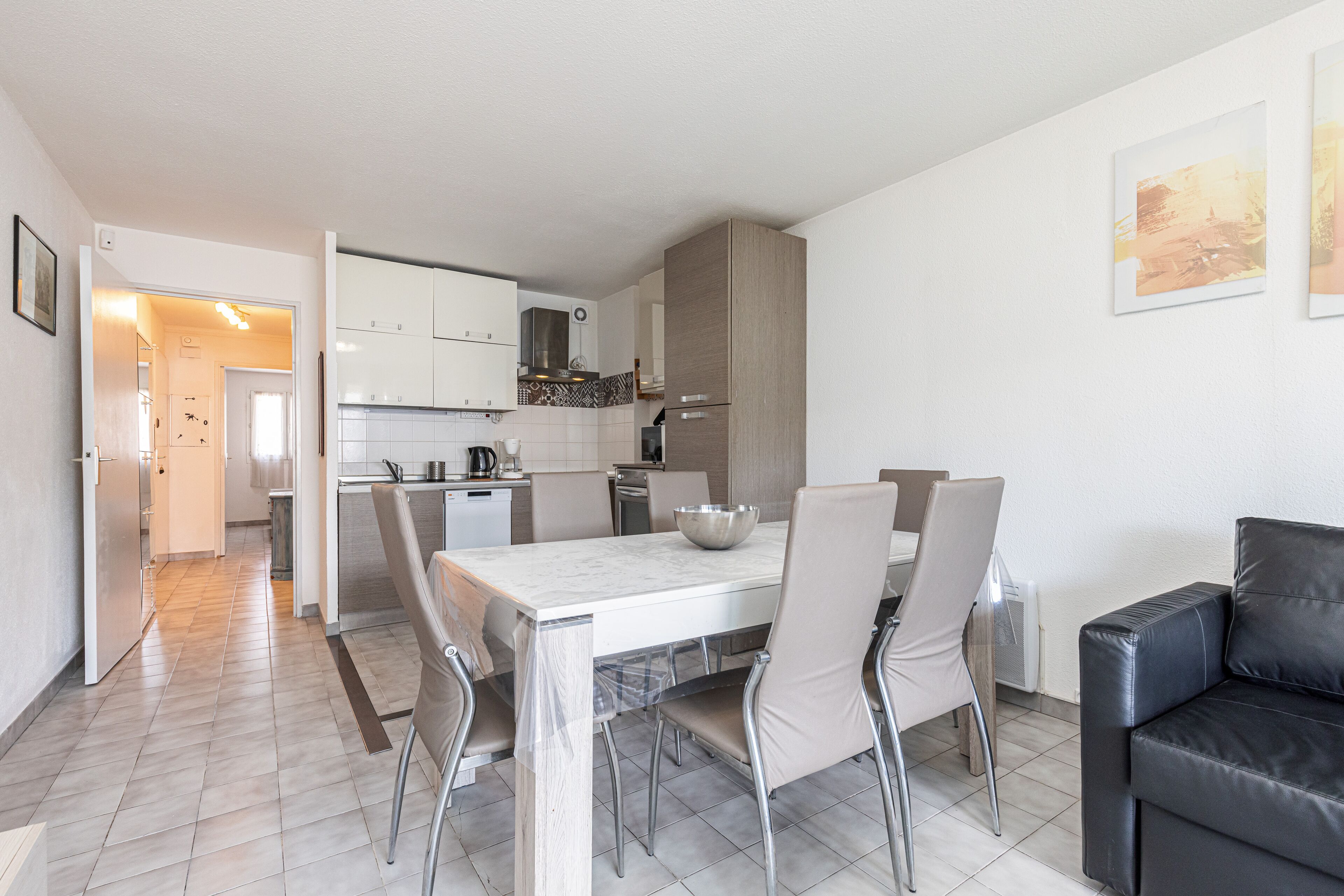 Una cocina moderna con armarios blancos, una mesa de comedor con sillas y un sofá de cuero negro.