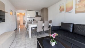 En moderne stue med en sort lædersofa, et spisebord med stole og et køkken i baggrunden.