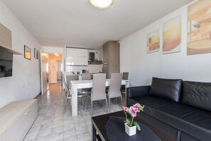 A modern living room with a black leather sofa, a dining table with chairs, and a kitchen in the background.