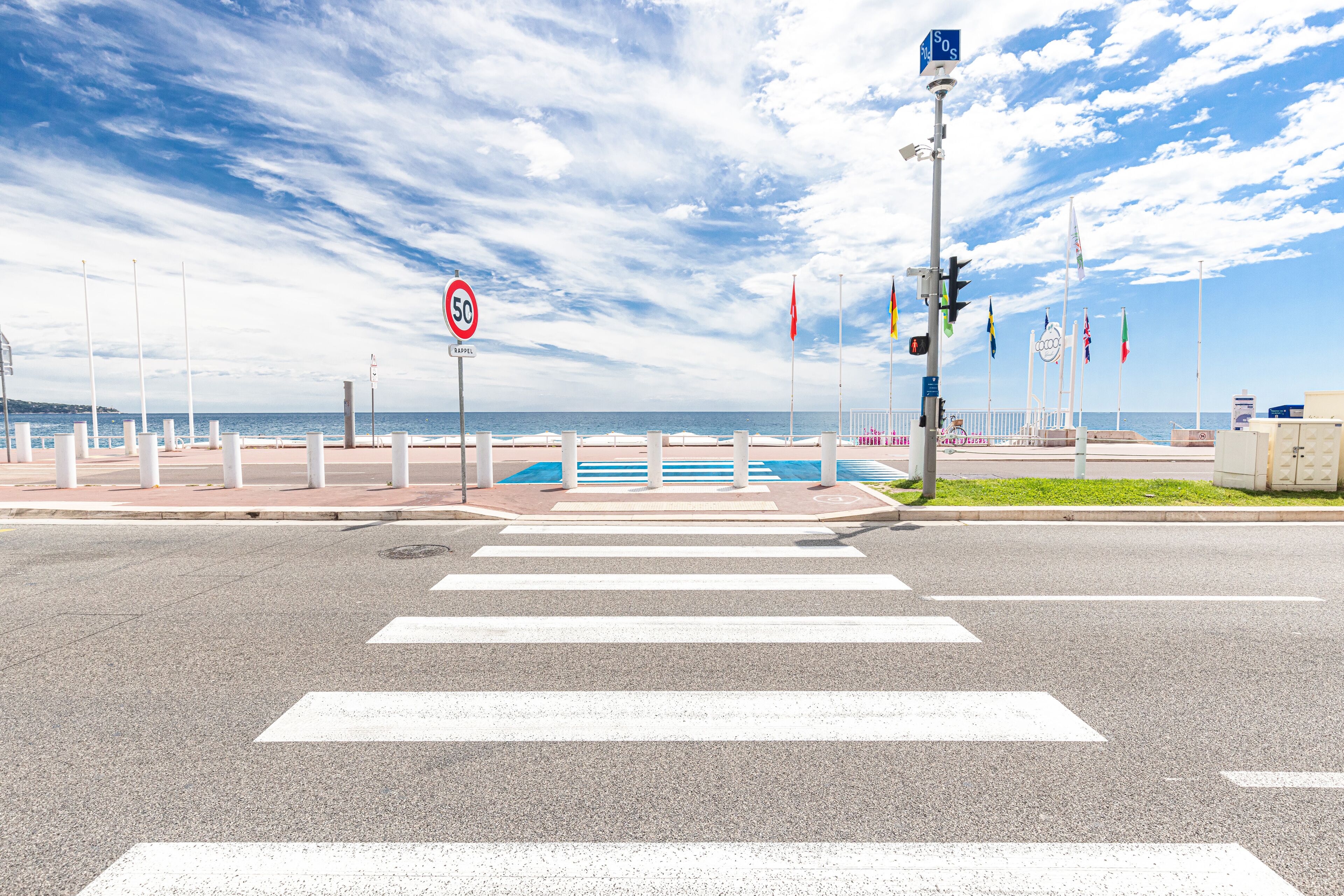 A pedestrian crossing with white stripes, a speed limit sign of 50 km/h, and multiple flags.