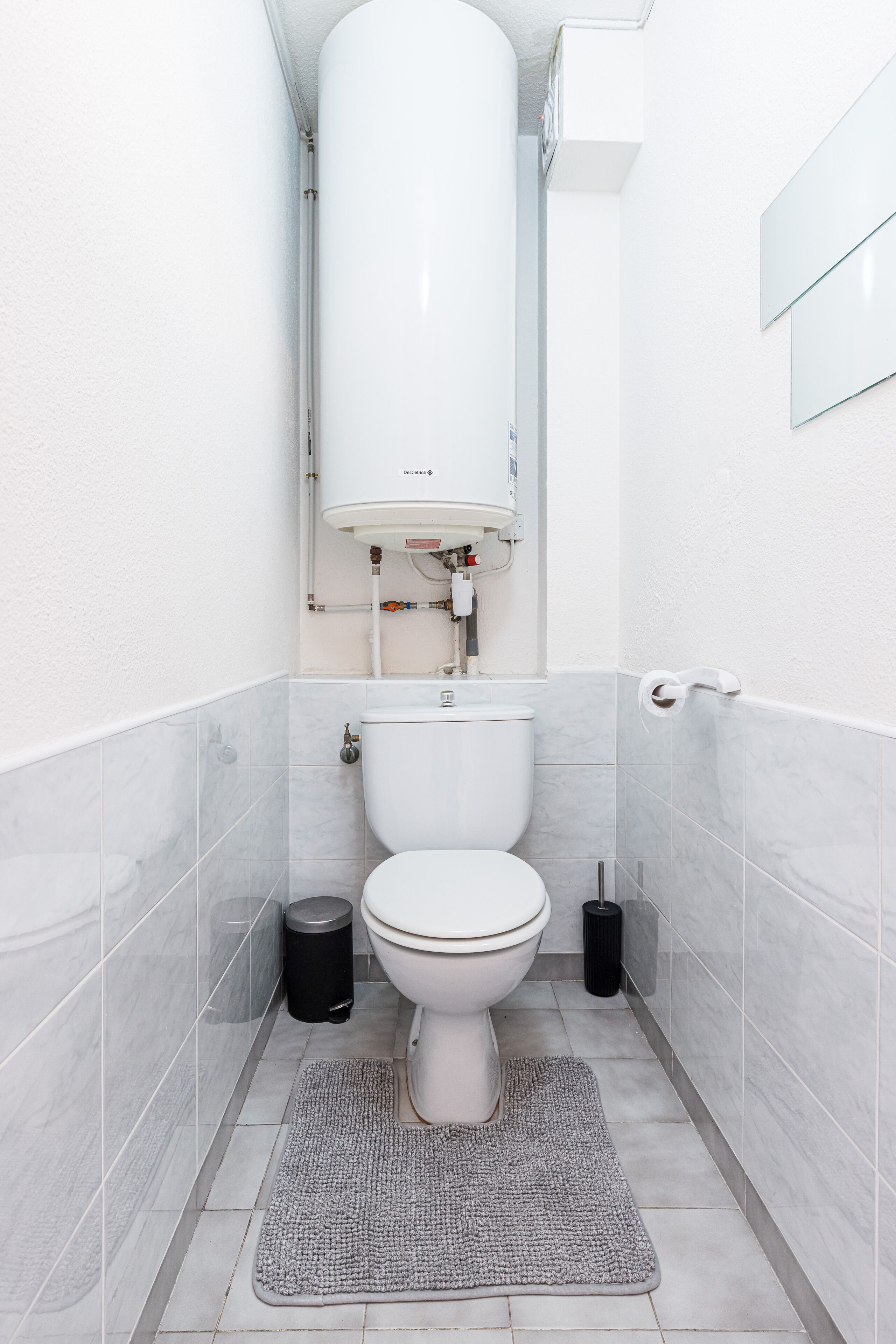 A modern bathroom with a toilet, a white tank, and a grey floor mat.