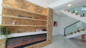 A modern interior with a stone wall fireplace, wooden shelves, and a staircase. - Shanyutianyuan (Huairou)