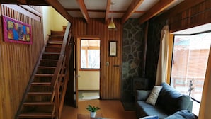 A wooden interior with a staircase, a sofa, and a stone wall.