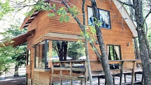 A wooden cabin with a deck, large windows, and a view of the surrounding trees.