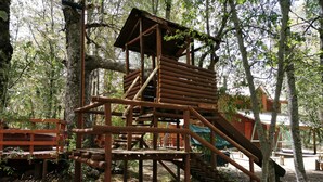 A wooden play structure with a slide and stairs, surrounded by trees.