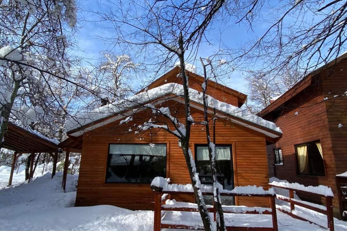 Eine Holzhütte mit verschneitem Dach und einer Holzterrasse davor.
