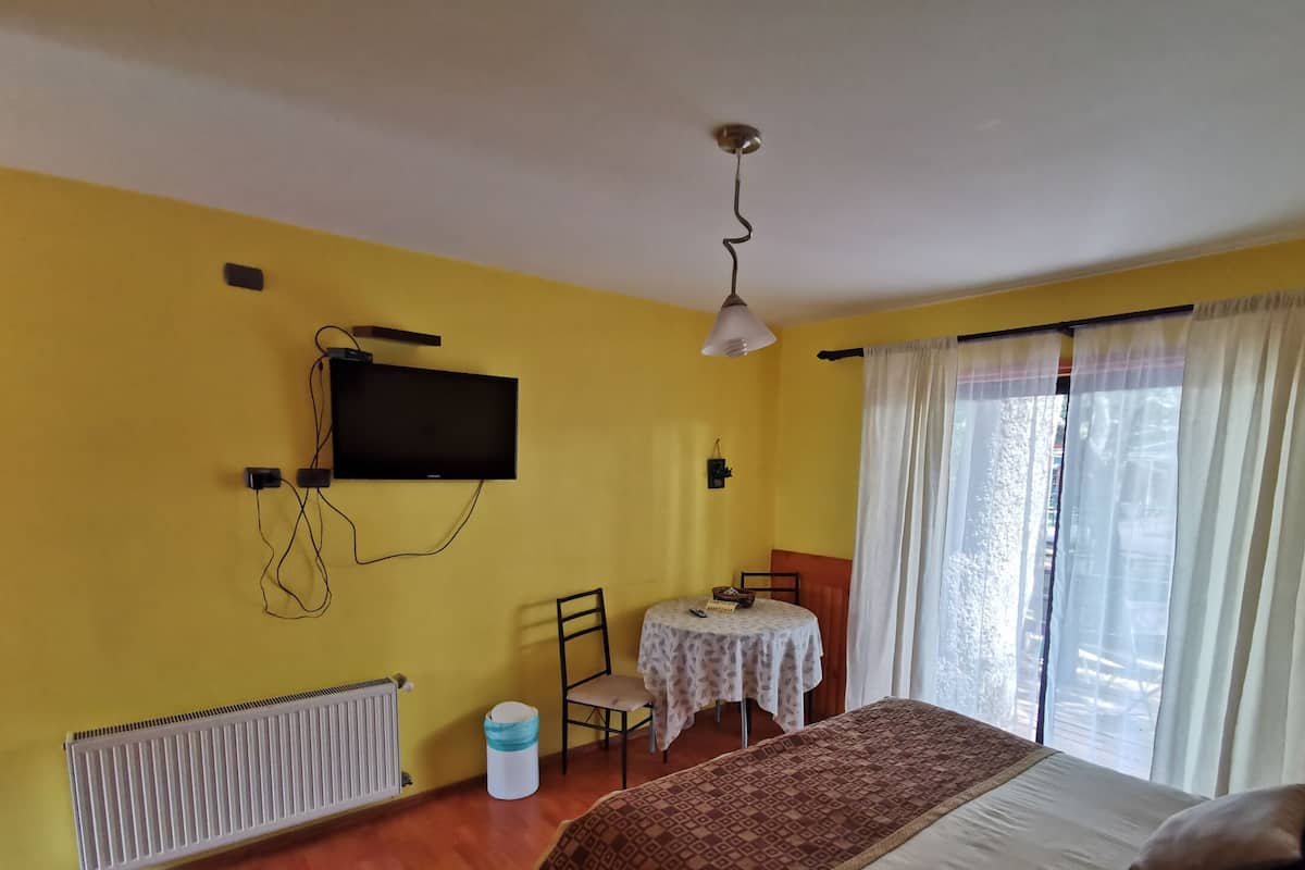 Ein Zimmer mit einem Bett, einem Schreibtisch mit Stuhl, einem an der Wand befestigten Fernseher und einem Fenster mit Vorhängen.