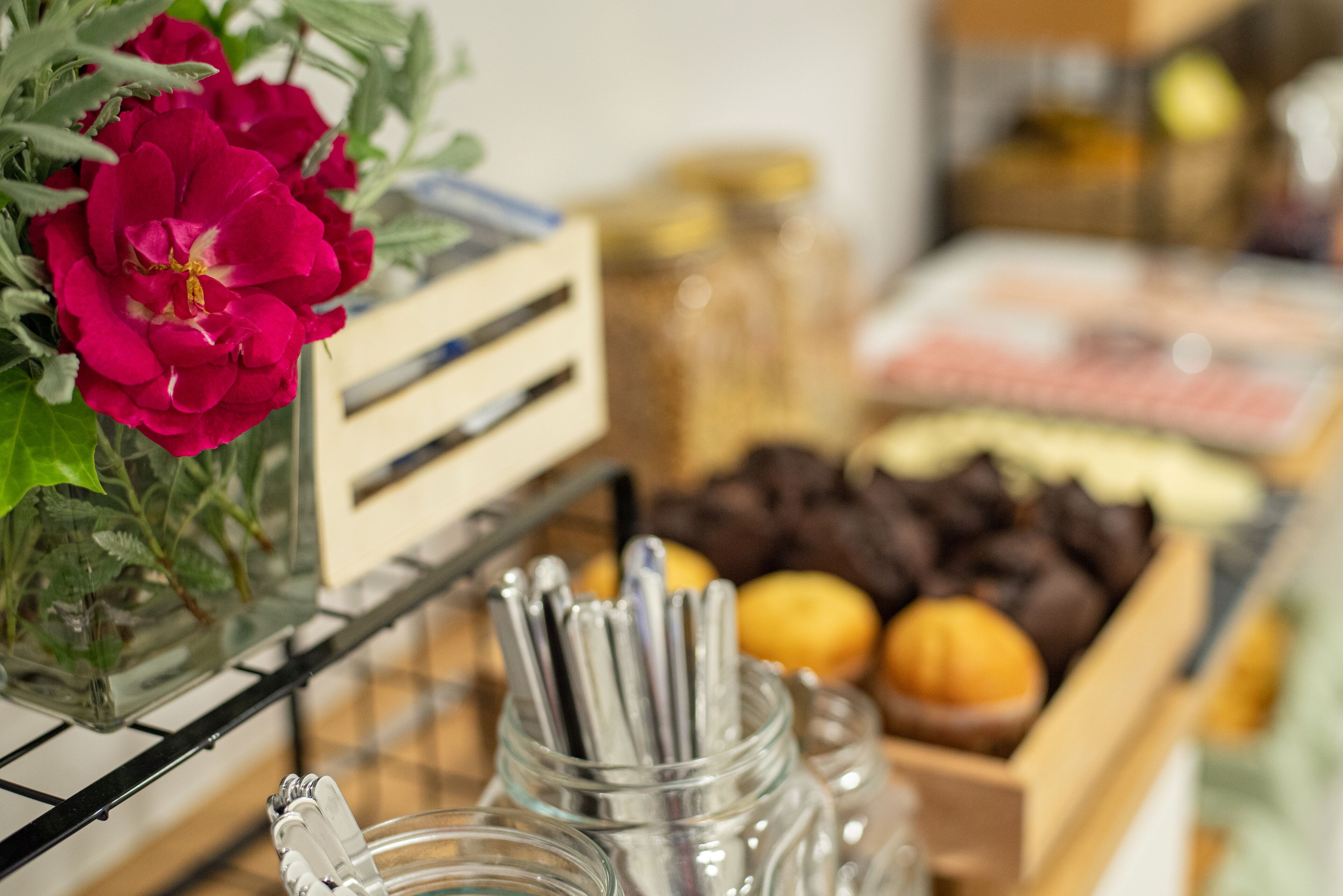 A buffet table with various food items, including pastries and fruits, and a vase with red flowers.