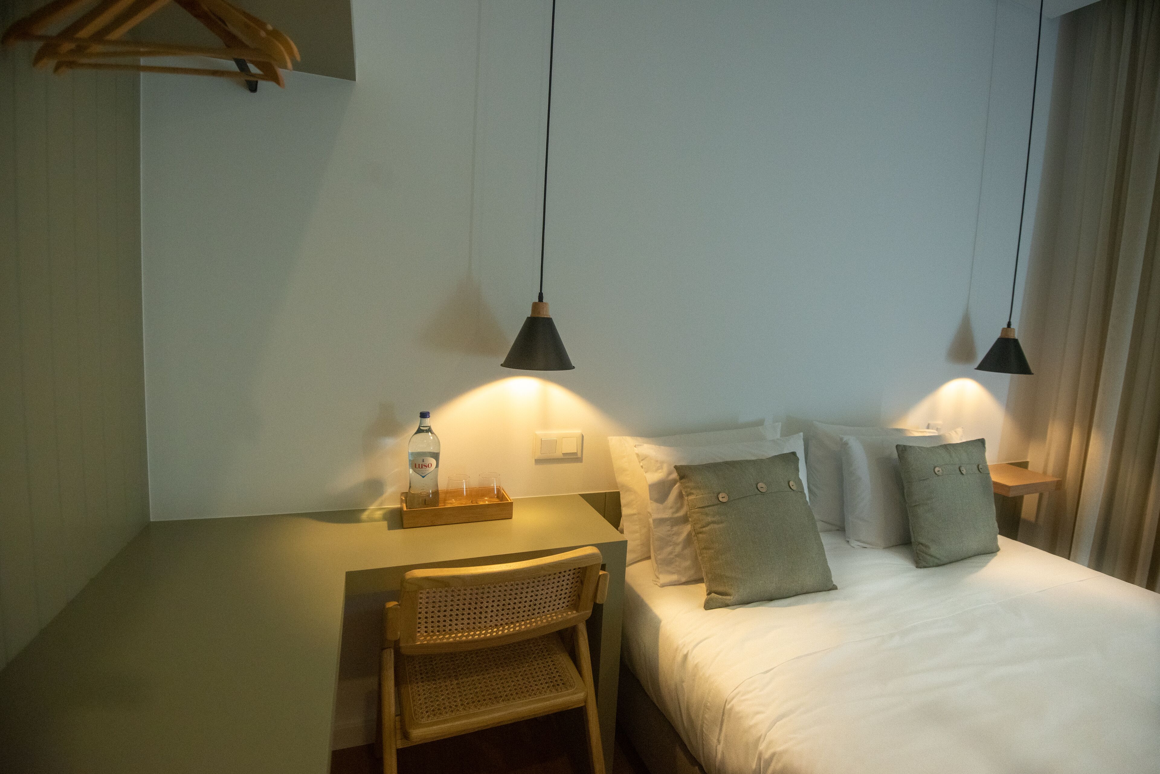 A hotel room with a bed, a desk, and two hanging lamps.