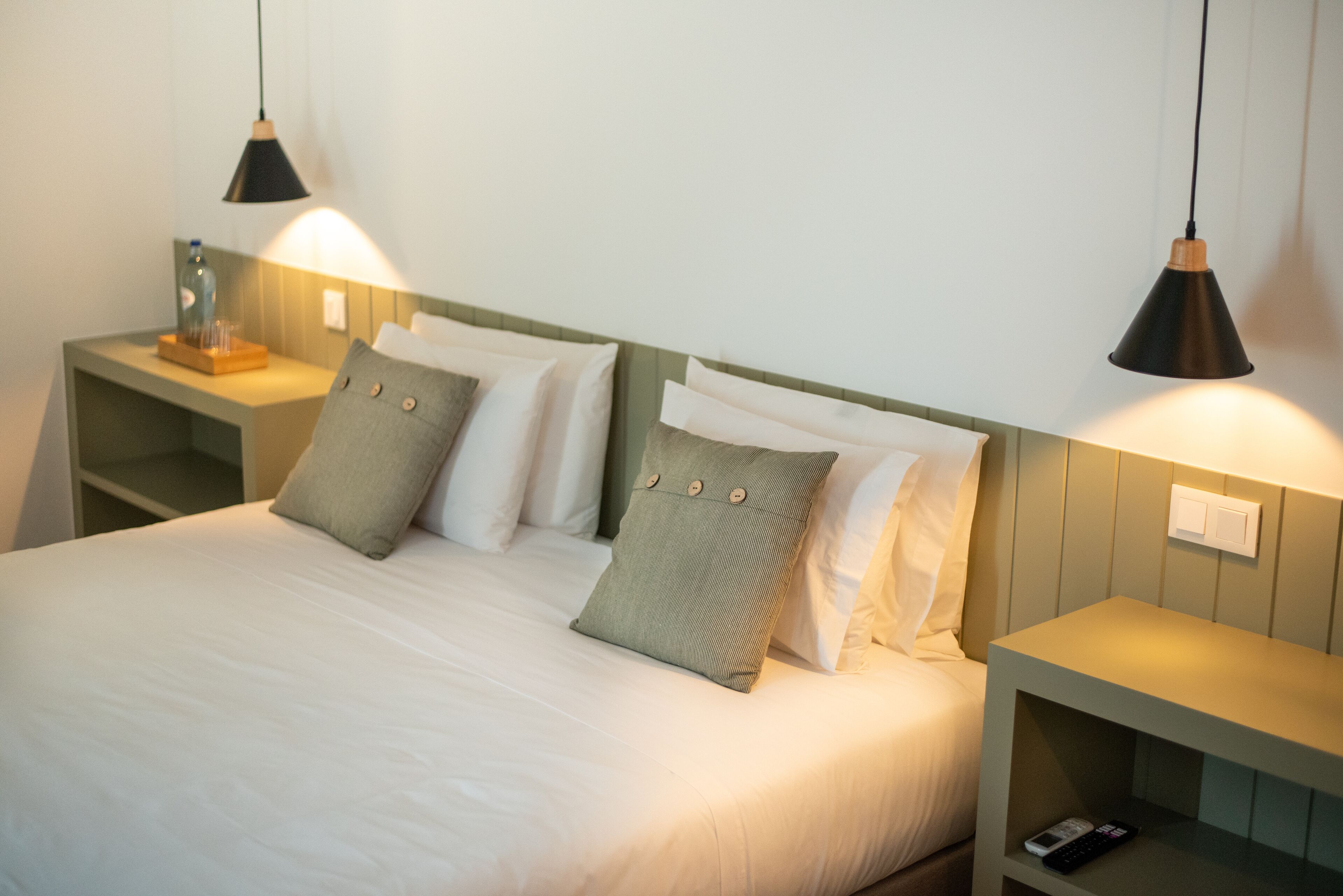 A neatly made bed with white linens, two bedside tables with lamps, and a remote control on one of the tables.