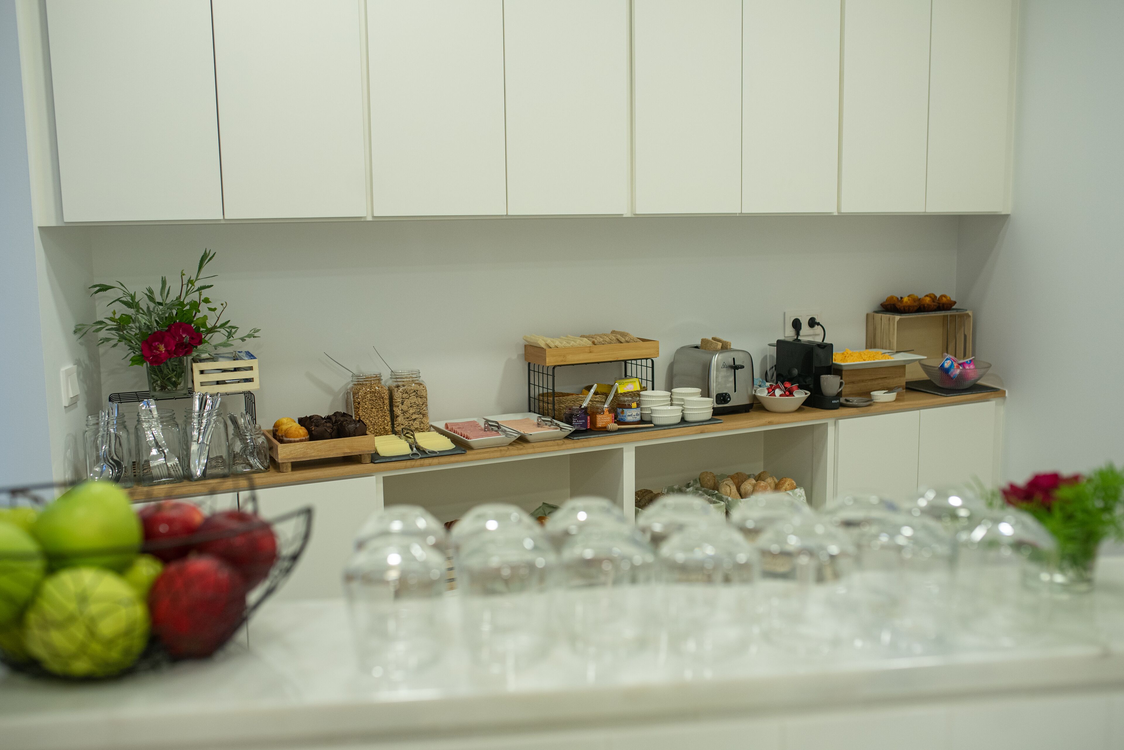 A kitchen counter with various food items, glassware, and a fruit bowl.
