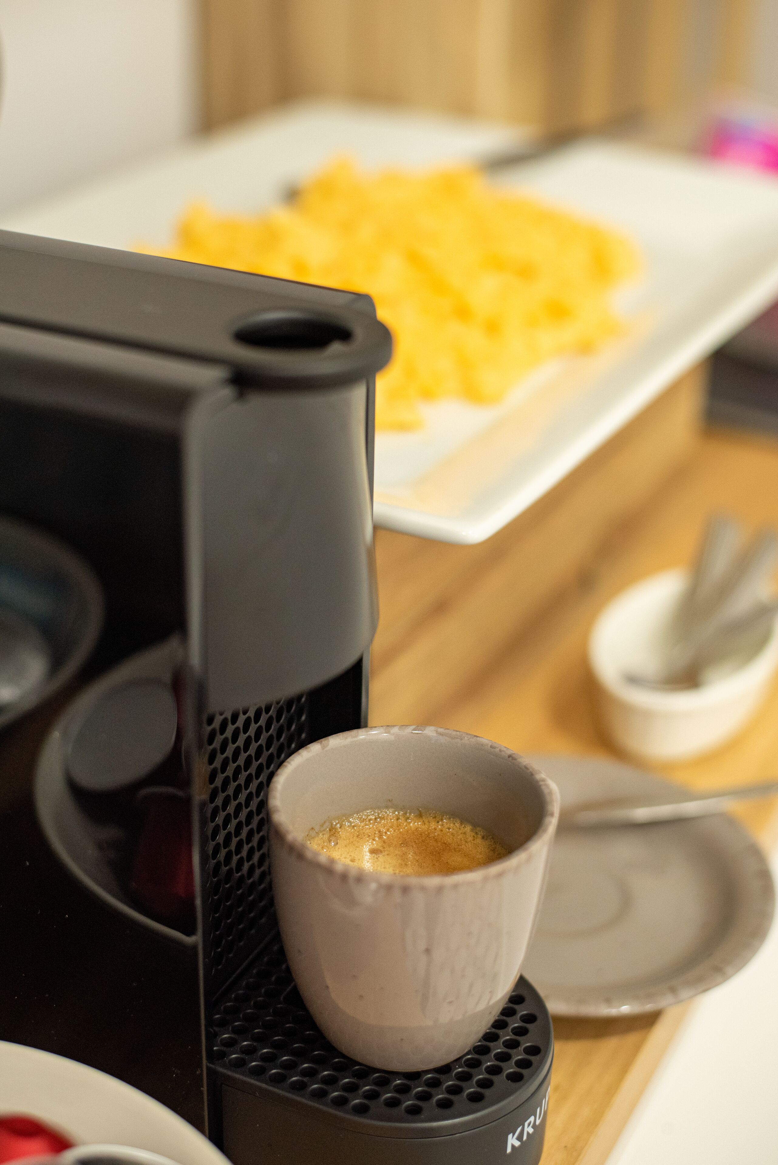 Een koffiezetapparaat met een kop koffie, een bord roerei en een kleine suikerkom in een keuken.