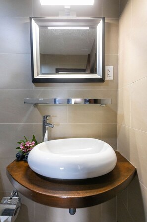 Un baño con un lavamanos blanco, un espejo y un perchero para toallas.