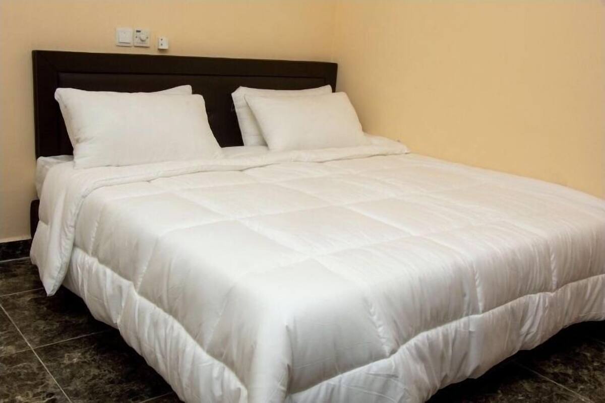 A neatly made bed with a dark headboard, white bedding, and a tiled floor.