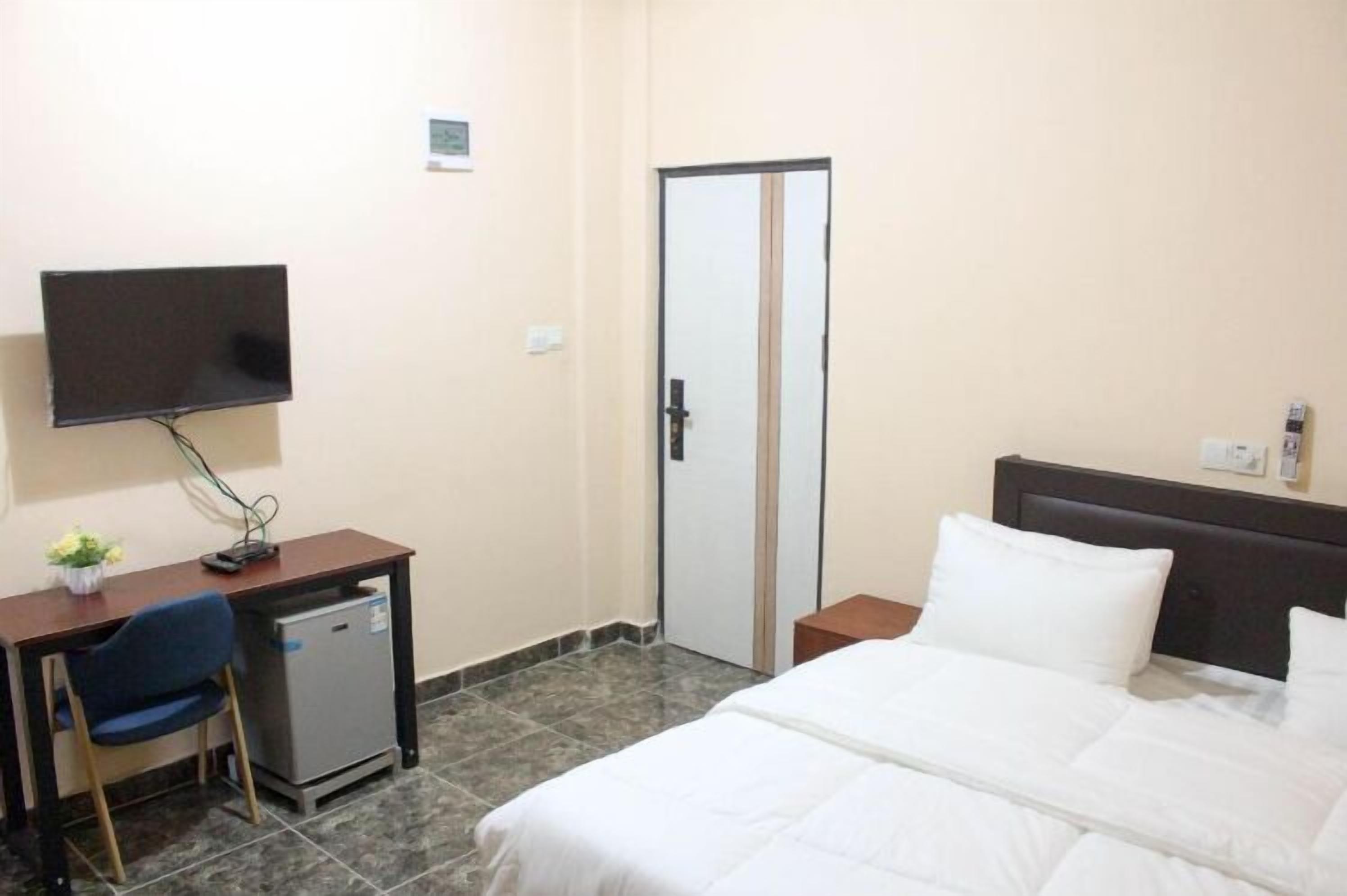 Une chambre d’hôtel avec un lit, un bureau avec un ordinateur, une télévision et une porte.