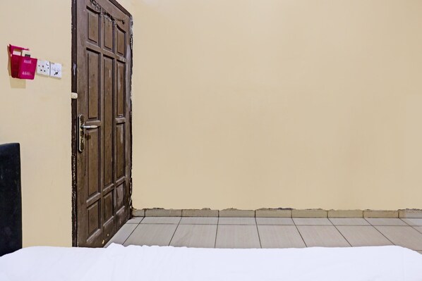 A room with a closed wooden door, a wall socket, and a tiled floor.