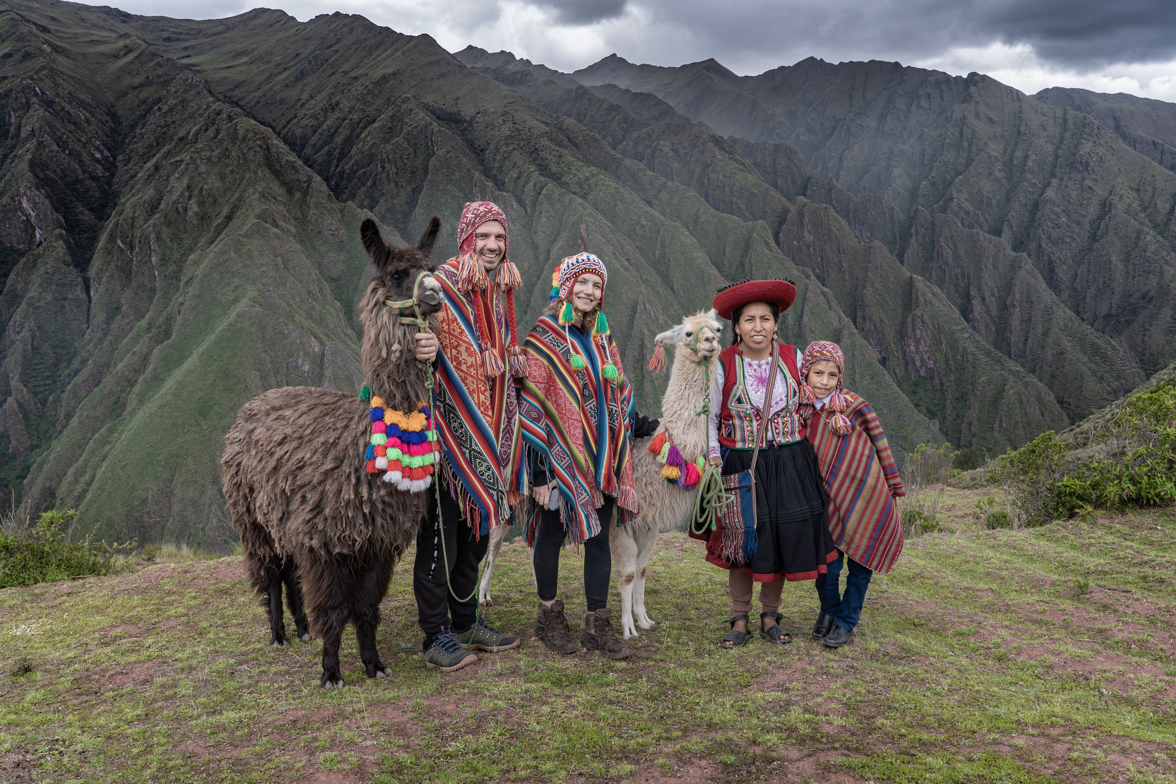 A group of people in traditional attire standing on a grassy hill with a mountainous backdrop.