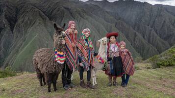 A group of people in traditional attire standing on a grassy hill with a mountainous backdrop.