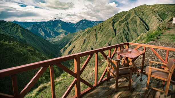 Terraza de madera con una mesa y sillas, con vistas a un paisaje montañoso.