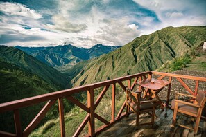 A wooden deck with a table and chairs overlooking a mountainous landscape. - Alpaca Lodge (Chinchero)
