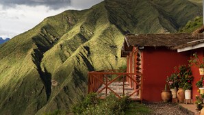 Un paisaje montañoso con un edificio rojo que tiene techo de paja y una escalera de madera que sube a un porche.