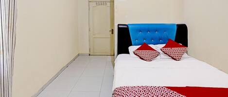 A hotel room with a bed, a blue headboard, and a red and white patterned bedspread.