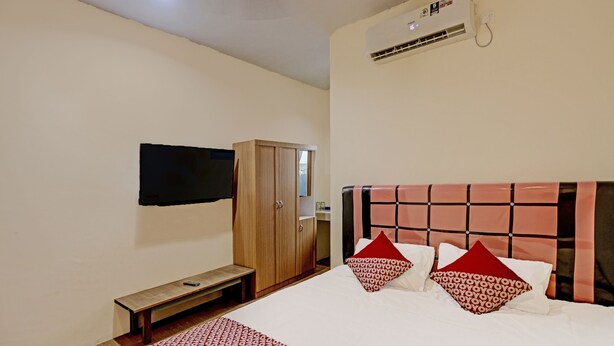 A hotel room with a bed, a wooden wardrobe, a bench, a flat-screen TV mounted on the wall, and an air conditioning unit. - Hotel O Aulia Homestay Syariah (Batam)