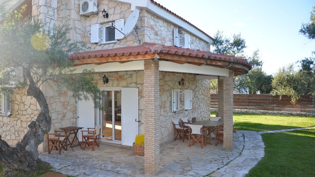 Une maison en pierre avec un patio, un espace salon extérieur et un arbre.