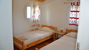 Une petite chambre agréable, dotée de deux lits simples, d’une fenêtre ornée de rideaux à motifs floraux, d’une table de chevet avec une lampe et d’un appareil de climatisation.