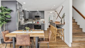 A modern kitchen with dark cabinets, a central island, and a dining area with wooden chairs and a table.