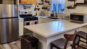Une cuisine moderne dotée d’un îlot central, d’appareils électroménagers en acier inoxydable, de planchers en bois et d’un mur au décor rustique.