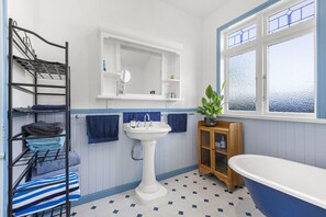 A bathroom with a sink, mirror, and bathtub. There is a shelf with towels and a plant. - Spacious, Welcoming, and Secure (Hamilton)