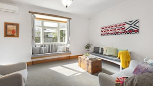 A modern living room with a large window, a sofa, a wooden coffee table, and a wall-mounted artwork. - Spacious, Welcoming, and Secure (Hamilton)