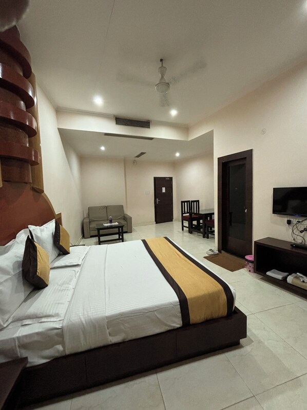 A hotel room with a large bed, a sofa, a TV, and a ceiling fan. - Hotel Akanksha (Jagdalpur)