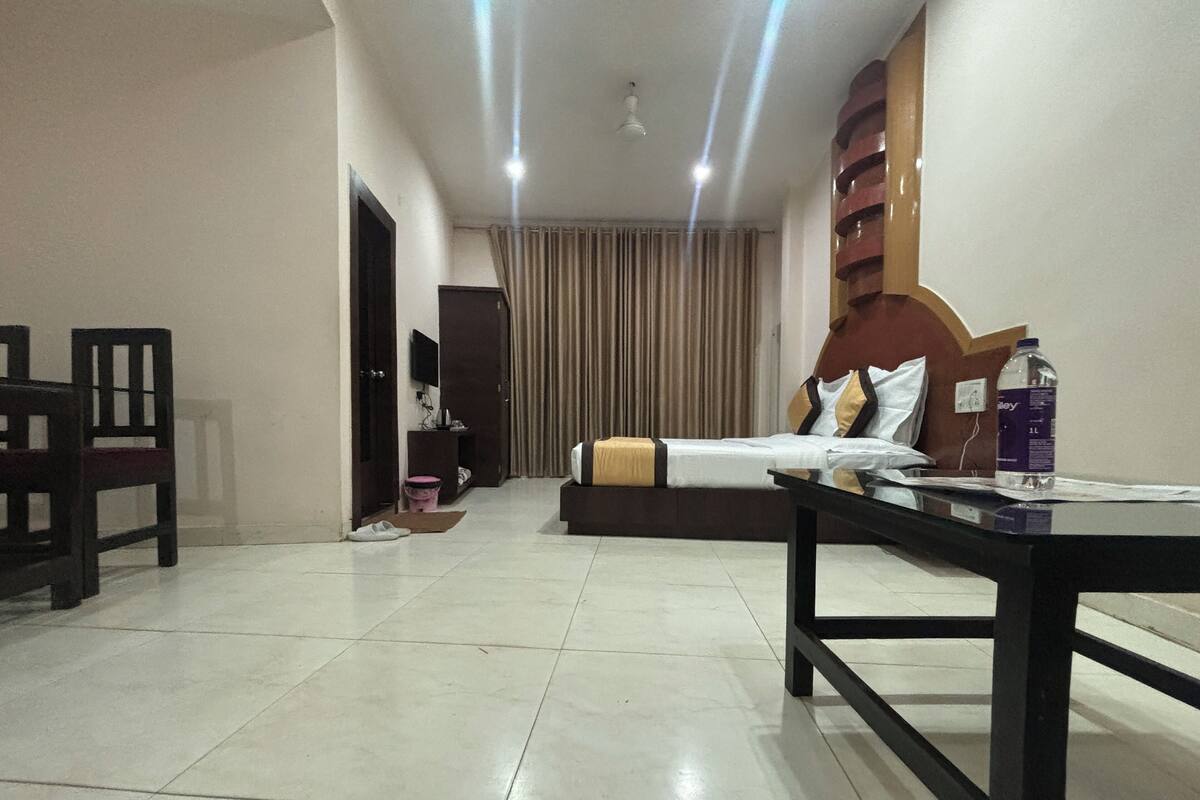 A hotel room with a bed, a desk, a chair, a TV, and a water bottle on the nightstand.