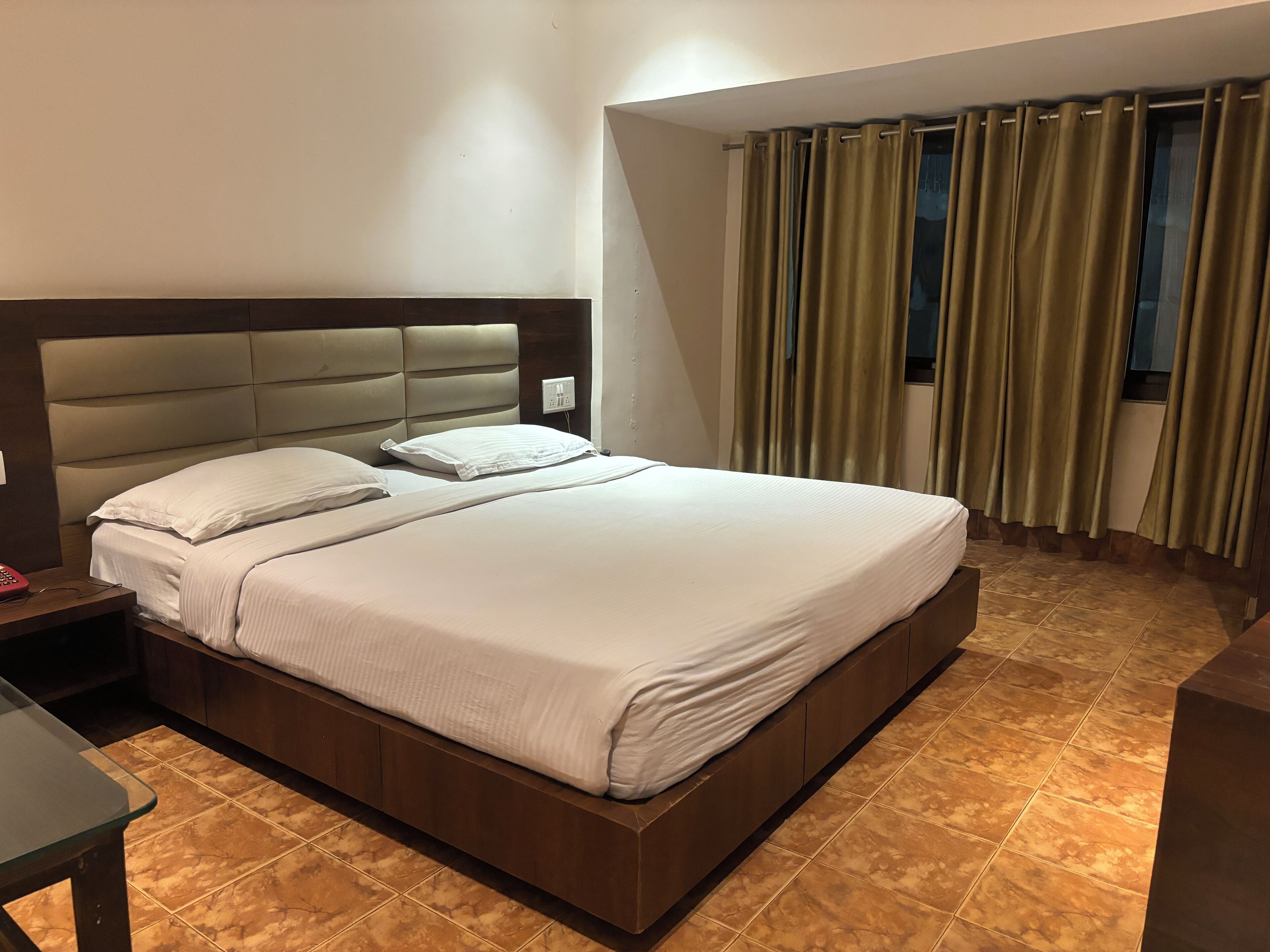 Une chambre d’hôtel avec un grand lit, une table de chevet, un bureau et une fenêtre avec des rideaux.