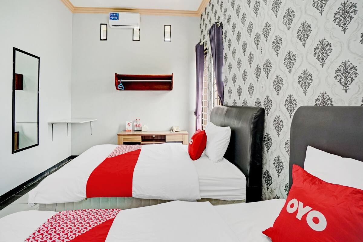 Une chambre d’hôtel avec deux lits, une table de chevet, un miroir, un climatiseur fixé au mur et un papier peint à motifs.