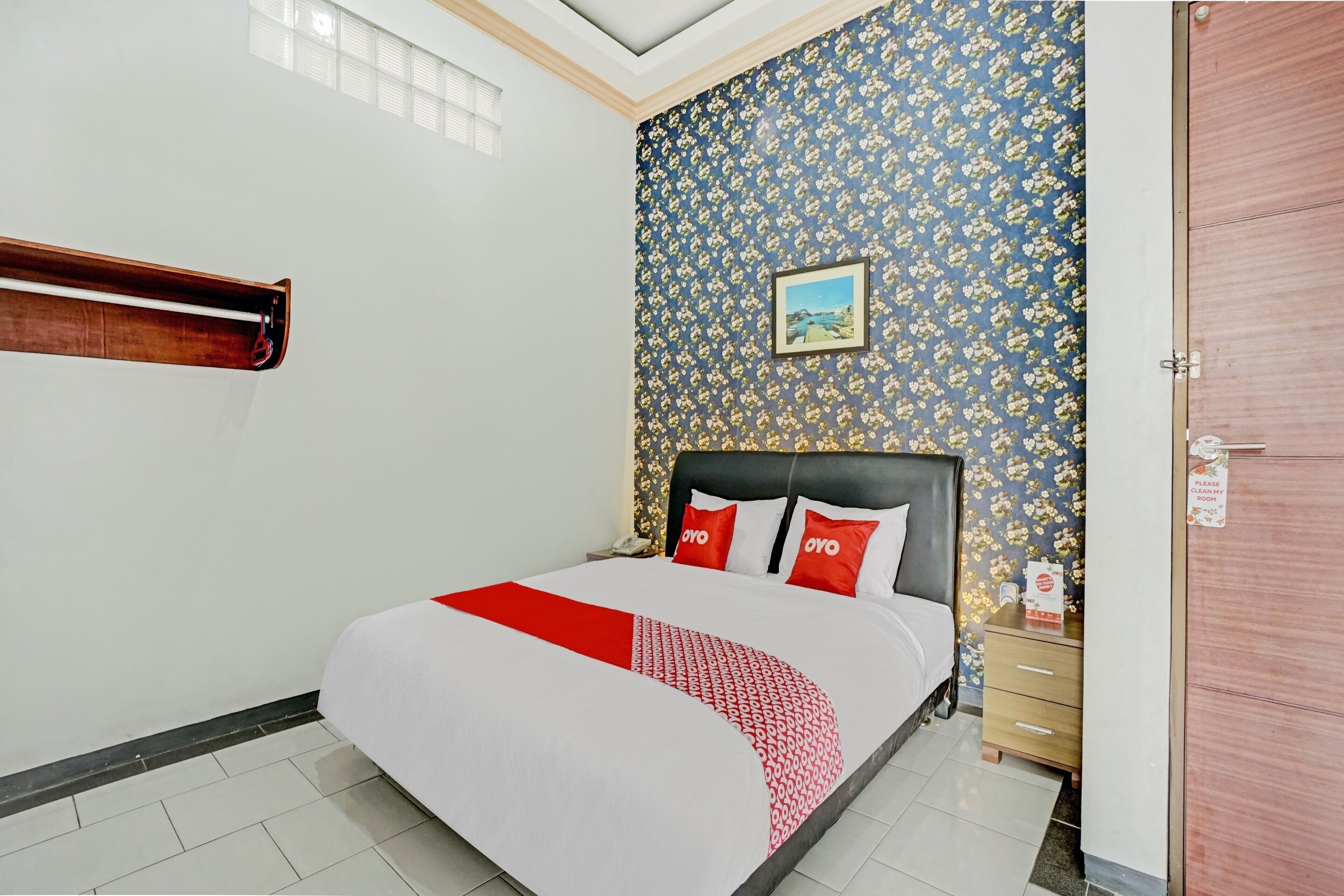 A hotel room with a bed, a nightstand, a wooden door, and a patterned wallpaper.