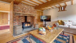 Una sala de estar acogedora con chimenea de ladrillo, vigas de madera, televisor, sofá y una mesa de centro con alfombra.