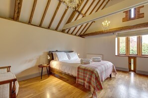 Ein Schlafzimmer mit Holzboden, einem Bett mit weißen Leinentüchern, einem Nachttisch mit einer Lampe und einem Fenster mit Jalousien.