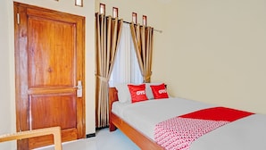A hotel room with a wooden door, a bed with red and white bedding, and a woven chair. - OYO Life 90472 Villa Dua Dua (Batu)