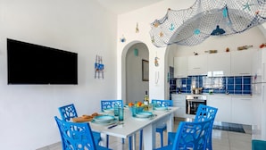 A modern kitchen with white cabinets, a dining table with blue chairs, and a TV mounted on the wall. - Casa Celeste 100m From Beach (Porto Cesareo)