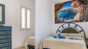 A bedroom with a bed, a dresser, a window, and a painting of a coastal scene. - Casa Celeste 100m From Beach (Porto Cesareo)