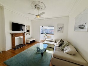 A living room with a fireplace, a sofa, a coffee table, a television, and a ceiling fan. - Sunny Apartment in Surry Hills (Surry Hills)