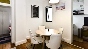 Un comedor con una mesa redonda y cuatro sillas, una lámpara colgante y una lista de ciudades enmarcada en la pared.