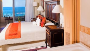 A hotel room with two beds, a balcony with a view of the sea, a wooden nightstand, and a large bathtub.